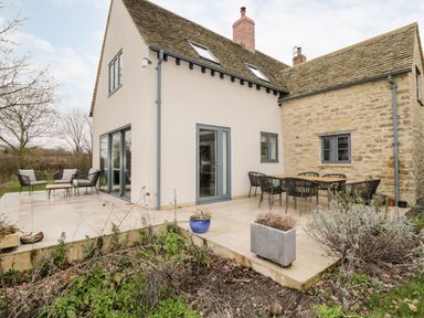 An outdoor patio with a dining table and chairs and outdoor seating beside a two-story house at High Cogges Farm Holiday Cottages in Witney