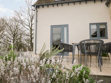 An outdoor patio area with a table and chairs surrounded by plants at High Cogges Farm Holiday Cottages Witney