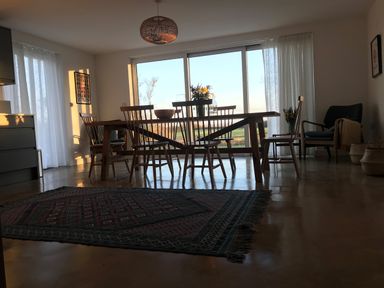 A dining room with a wooden table and chairs a rug on the floor and large sliding glass doors at High Cogges Farm Holiday Cottages in Witney