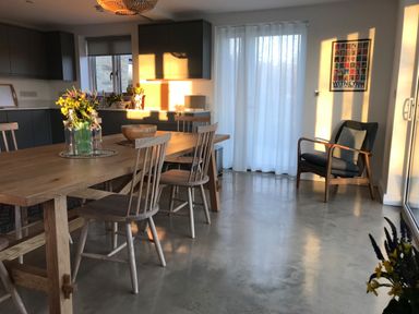 A kitchen and dining area with wooden table and chairs a gray armchair and a window covered by white curtains at High Cogges Farm Holiday Cottages Witney