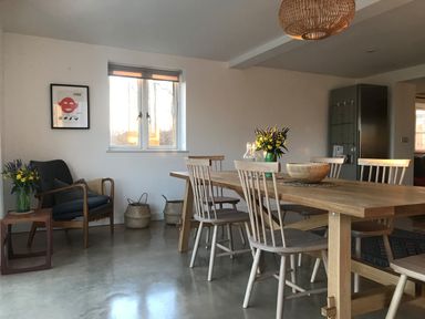 A dining room with a wooden table and chairs a blue armchair with a side table and flowers at High Cogges Farm Holiday Cottages in Witney