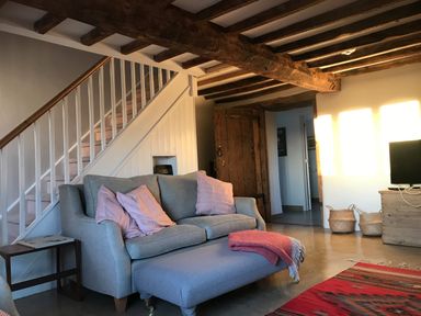 A living room with a grey sofa and pink cushions under wooden beam ceiling at High Cogges Farm Holiday Cottages Witney