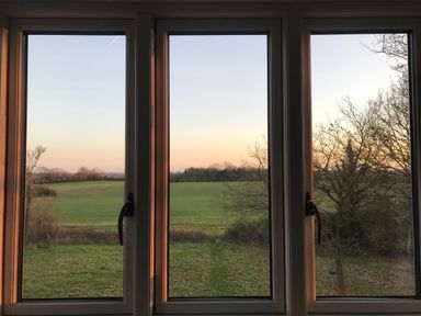 A view of green fields and trees through three windows at High Cogges Farm Holiday Cottages Witney