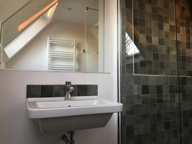 A bathroom with a white sink and faucet a mirror a tiled shower wall and a wall-mounted towel radiator at High Cogges Farm Holiday Cottages Witney