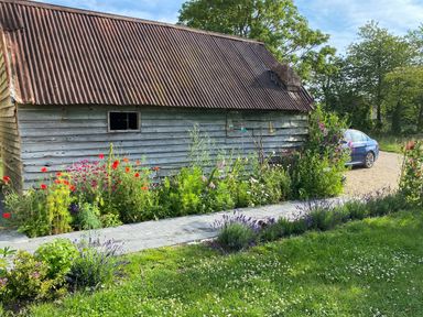 A garden with flowers next to a wooden shed and a blue car at High Cogges Farm Holiday Cottages in Witney