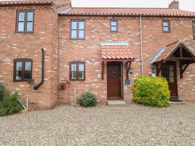 A brick house exterior with two brown doors and four windows with gravel in front at 10 Ruston Reaches East Ruston near Stalham