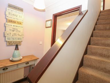 A staircase next to a wooden table with a vase and decorative sign on the wall at 10 Ruston Reaches East Ruston near Stalham