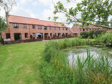 A row of brick houses with tiled roofs by a pond and grassy area at 10 Ruston Reaches in East Ruston near Stalham