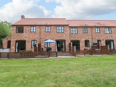 A rear view of terraced brick houses with fenced patios and outdoor furniture on a lawn at 10 Ruston Reaches in East Ruston near Stalham