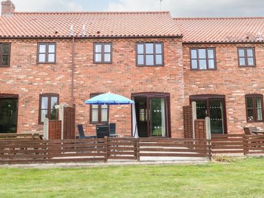 A brick terraced house with wooden fencing a patio table with chairs and a blue umbrella at 10 Ruston Reaches East Ruston near Stalham