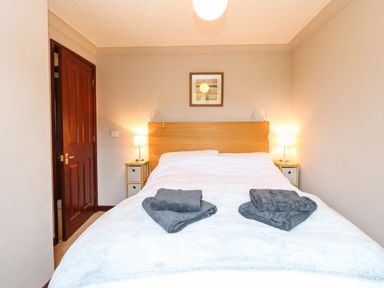 A bedroom with a double bed towels on the bed lamps on bedside tables and a wooden door at 10 Ruston Reaches East Ruston near Stalham