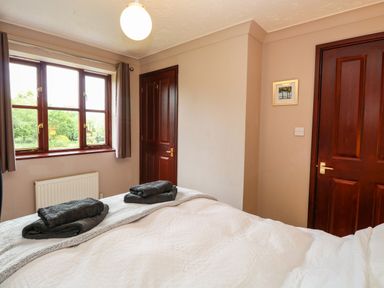 A bedroom with a bed with folded towels there are two wooden doors and a window showing trees outside at 10 Ruston Reaches East Ruston near Stalham