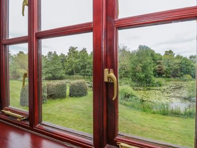 A window with wooden frames overlooking a garden with trimmed bushes and a pond with lily pads at 10 Ruston Reaches East Ruston near Stalham