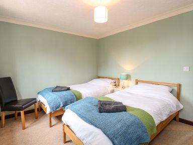 A bedroom with two single beds blue and green blankets and a black chair at 10 Ruston Reaches East Ruston near Stalham