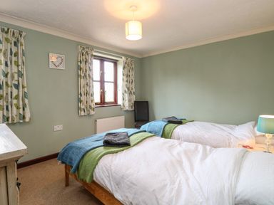 A bedroom with two single beds with white bedding and blue and green throws at 10 Ruston Reaches East Ruston near Stalham