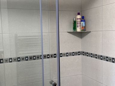 A tiled shower corner with black and gray decorative border tiles and three bottles on a corner shelf at 10 Ruston Reaches East Ruston near Stalham