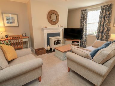 A living room with two beige sofas around a wooden coffee table near a fireplace a TV on a stand and patterned curtains at Charter's Cottage in Berwick-Upon-Tweed