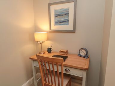 A wooden desk with a chair a lamp a clock a small box a mug and a picture on the wall at Charter's Cottage in Berwick-Upon-Tweed