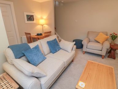 A living room with beige sofa with blue cushions armchair with yellow cushion coffee table and small dining table with lamp at Charter's Cottage in Berwick-Upon-Tweed