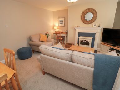 A living room with a couch, armchair, desk with chair, coffee table, fireplace, TV, and decorative items at Charter's Cottage in Berwick-Upon-Tweed