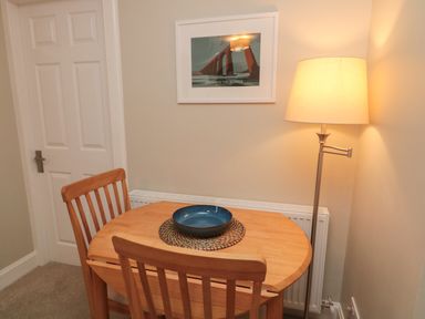 A small wooden dining table with two chairs a blue bowl a floor lamp and a framed picture on the wall at Charter's Cottage in Berwick-Upon-Tweed