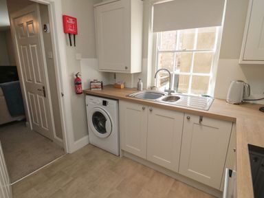A kitchen with a washing machine under the counter a sink under a window and a kettle on the counter at Charter's Cottage in Berwick-Upon-Tweed