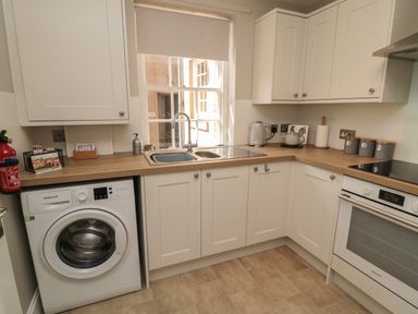 A kitchen with white cabinets a washing machine a sink a kettle and an oven at Charters Cottage in Berwick-Upon-Tweed