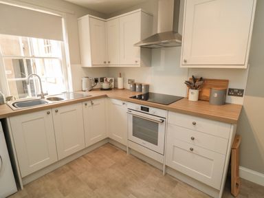 A kitchen with white cabinets a wooden countertop an electric stove a sink and kitchen utensils at Charter's Cottage in Berwick-Upon-Tweed