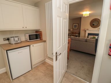 A kitchen area with a toaster microwave mini fridge and cabinets opening to a living room with a sofa and a fireplace at Charter's Cottage in Berwick-Upon-Tweed