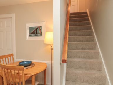 A carpeted staircase next to a wooden dining table with chairs a lamp and a framed picture on the wall at Charter's Cottage in Berwick-Upon-Tweed