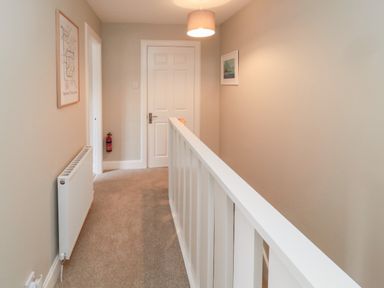 A hallway with beige walls and carpet next to a white staircase railing at Charter's Cottage in Berwick-Upon-Tweed
