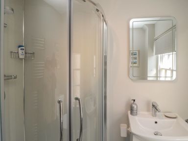 A bathroom with a glass shower enclosure and a white sink with a mirror above at Charter's Cottage Berwick-Upon-Tweed