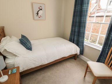 A bedroom with a single bed wooden chair bedside table and window with blue curtains at Charters Cottage in Berwick-Upon-Tweed