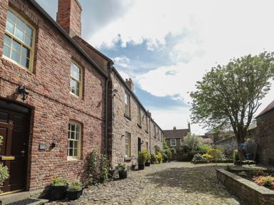 A cobblestone courtyard with brick and stone houses and potted plants at Charter's Cottage in Berwick-Upon-Tweed