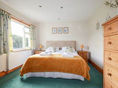 A bedroom with double bed with yellow blanket bedside tables lamps and wooden dresser at Brookfield in St Gennys near Wainhouse Corner