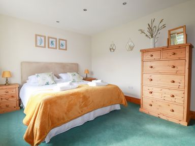 A bedroom with a double bed bedside tables lamps a wooden chest of drawers and wall decorations at Brookfield in St Gennys near Wainhouse Corner