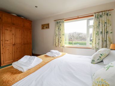 A bedroom with a bed folded towels wooden wardrobe and window with floral curtains at Brookfield in St Gennys near Wainhouse Corner