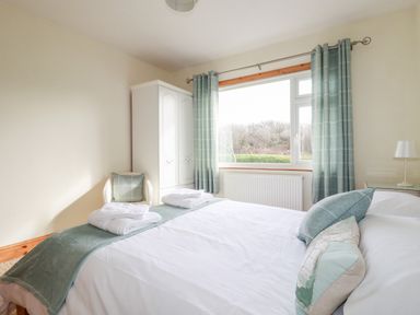 A bedroom with a bed pillows folded towels a white wardrobe a chair and a window with curtains at Brookfield in St Gennys near Wainhouse Corner