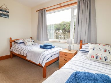 A bedroom with two single wooden beds striped bedding towels on beds a wooden bedside table lamp and a window with curtains at Brookfield in St Gennys near Wainhouse Corner
