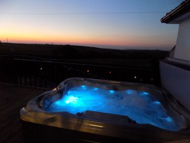 A hot tub with blue lights on a wooden deck at sunset at Brookfield in St Gennys near Wainhouse Corner