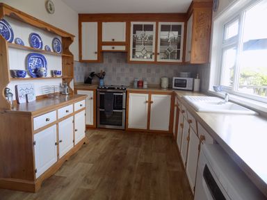 A kitchen with wooden and white cabinets a stove a sink and blue decorative plates on a wooden shelf at Brookfield in St Gennys near Wainhouse Corner