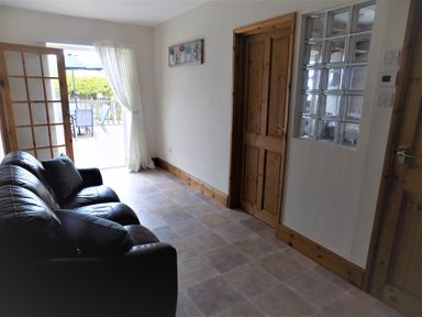A room with a black leather sofa next to a wooden door and glass block window at Brookfield in St Gennys near Wainhouse Corner