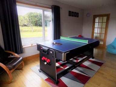 A room with a ping pong table on a geometric rug near a window with curtains and a chair at Brookfield in St Gennys near Wainhouse Corner