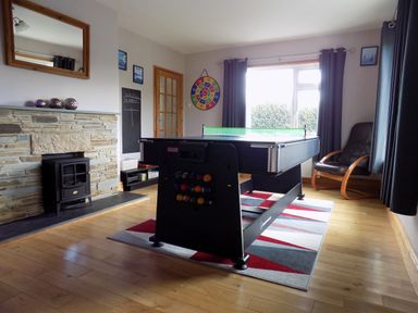 A game room with a pool table, dart board, armchair, and fireplace at Brookfield in St Gennys near Wainhouse Corner