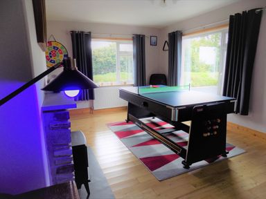 A game room with a table tennis and pool table on a rug and a dartboard on the wall at Brookfield in St Gennys near Wainhouse Corner