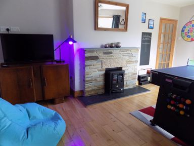 A living room with a television on a wooden cabinet a blue bean bag a stone fireplace and a ping pong table at Brookfield in St Gennys near Wainhouse Corner