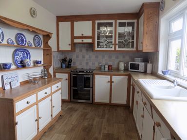 A kitchen with wooden cabinets white countertops a sink a stove a microwave and blue and white dishes on shelves at Brookfield St Gennys near Wainhouse Corner