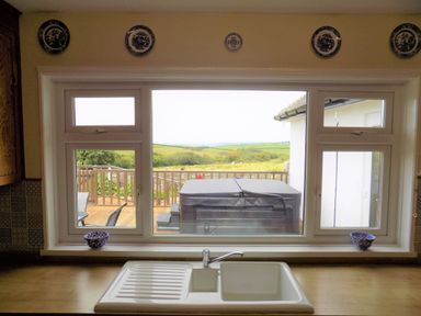 A kitchen sink with a wooden countertop and window looking out onto a wooden deck and green countryside at Brookfield in St Gennys near Wainhouse Corner