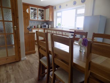A kitchen with wooden chairs around a table and kitchen cabinets with a refrigerator at Brookfield in St Gennys near Wainhouse Corner
