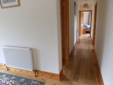 A hallway with wooden flooring and white walls leading to a bedroom at Brookfield in St Gennys near Wainhouse Corner